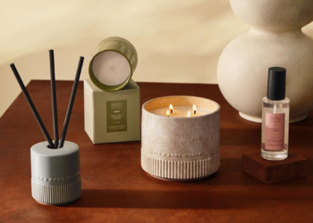 Bath & Body Works Reserve Collection products styled on a wooden table, including a lit three-wick candle, a reed diffuser, a boxed Sea Salt + Musk candle and a Vanilla + Tonka room mist.