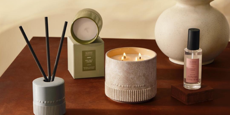 Bath & Body Works Reserve Collection products styled on a wooden table, including a lit three-wick candle, a reed diffuser, a boxed Sea Salt + Musk candle and a Vanilla + Tonka room mist.