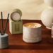 Bath & Body Works Reserve Collection products styled on a wooden table, including a lit three-wick candle, a reed diffuser, a boxed Sea Salt + Musk candle and a Vanilla + Tonka room mist.